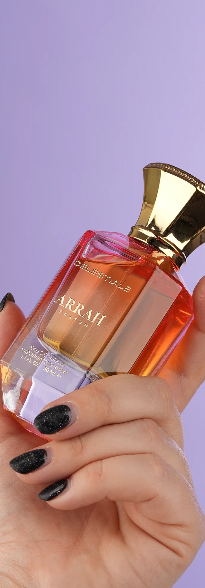 Hand holding a perfume bottle with a gold cap against a purple background